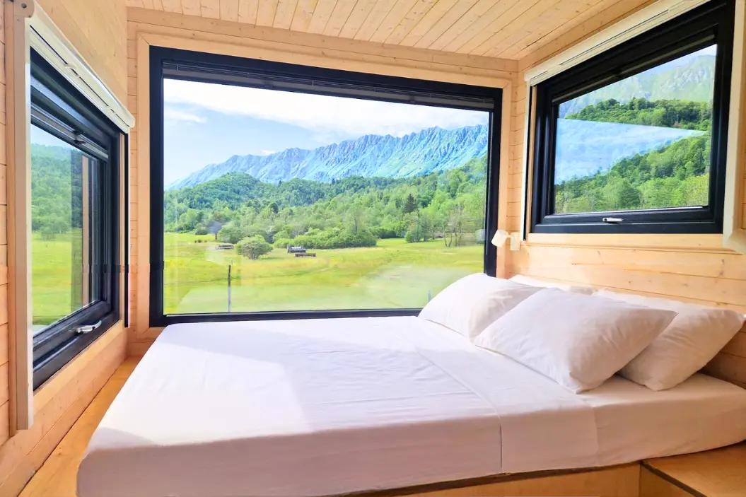Detailansicht der Fenster neben dem Bett im Tiny House Faggio mit Blick auf die Gipfel und Wälder